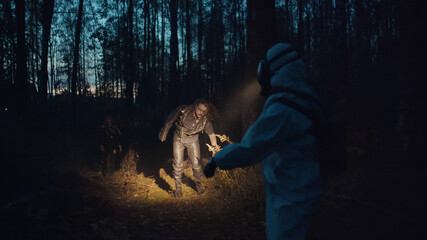 Two zombies in mysterious landscape attacking human in biohazard suit