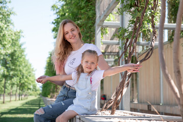 Beautiful mother and little daughter walking together in summer park