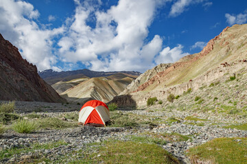 Bright tent in mountains under sunny blue sky.