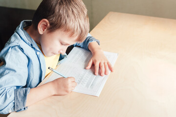Close up of cute boy doing his homework. Kid writing different lines with pencil. Children education concept.