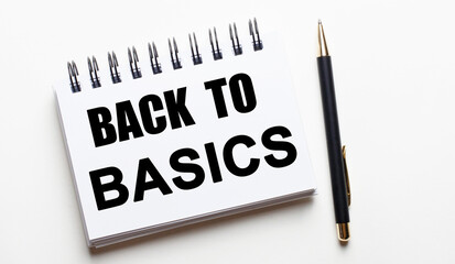 On a light background, a white notebook with the words BACK TO BASICS and a pen.