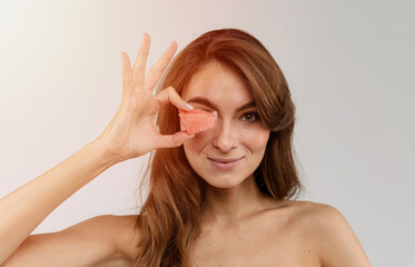 Young beautiful woman holding a piece of a watermelon in her hand near the eye, close up portrait isolated on white background