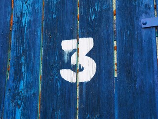 Number three on an old abandoned weathered blue colour wooden gate in Budapest suburb, Hungary