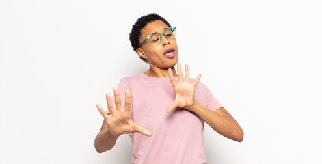 afro young black woman feeling terrified, backing off and screaming in horror and panic, reacting...