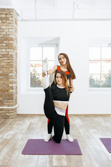 Fototapeta na wymiar two athletic young girls are stretching in a bright room for fitness wearing sports tight-fitting suits. one athlete helps another to do yoga exercises.