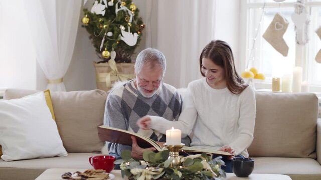 Young woman with grandfather indoors at home at Christmas, looking at photo album.