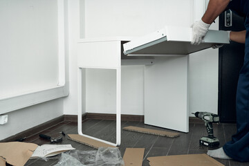 Furniture assembly process. Worker in overalls and white footwear. Installation of a drawer. Do it yourself.