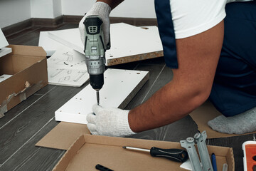 Furniture assembly process. Worker in overalls and white footwear. Using a cordless drill, screwdriver. Do it yourself.