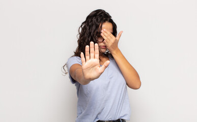pretty young woman covering face with hand and putting other hand up front to stop camera, refusing...