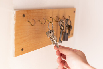 Man taking door key from wooden key holder hanging on the white wall, close up shot of male's hand