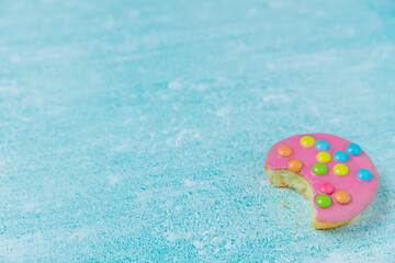 Pink glazed cookies on a blue background/surface. Dutch  cookies called Confettinis. It's a flat cake with pink fondant glazing and sprinkles.