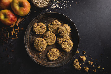 Freshly baked apple, oatmeal, raisin, cinnamon and mixed nuts cookies with ingredients on a dark concrete surface. Room for text.