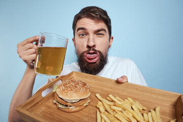 Cheerful man beer mug hamburger french fries fast food diet blue background close-up