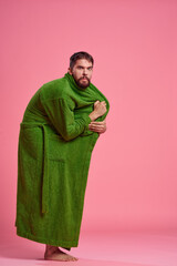 Fototapeta premium An emotional man in a green robe in full growth on a pink background gestures with his hands to the model