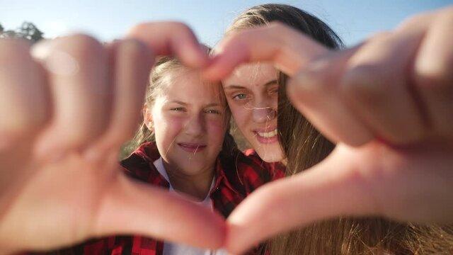 happy family in the park. two sisters show a heart symbol with their hands smiling. young mom and daughter show heart gesture with fingers. concept people in lifestyle the park happy family