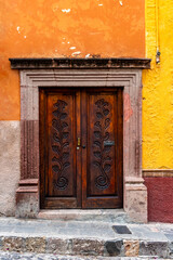 A vintage carved big double door  with a stone frame and a orange and yellow wall	