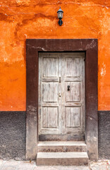 An old white washed wooden door with a brown frame and an orange wall