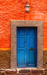 An old blue painted door with a fish knocker, stone frame and bright rough orange wall