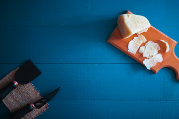 Composed cloesup detail view of aged cheddar cheese with cheese knife set, over vintage blue wooden backdrop, copy space includes