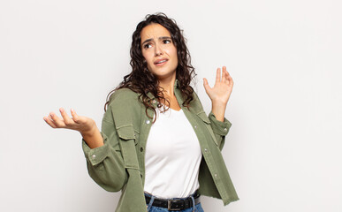pretty young woman shrugging with a dumb, crazy, confused, puzzled expression, feeling annoyed and...