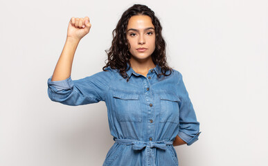 pretty young woman feeling serious, strong and rebellious, raising fist up, protesting or fighting...