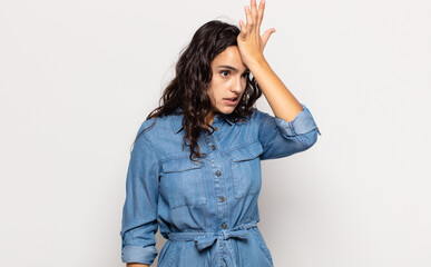 pretty young woman raising palm to forehead thinking oops, after making a stupid mistake or...