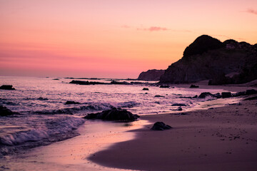 Obraz premium Beautiful sunset on a pristine beach with rocks in the background