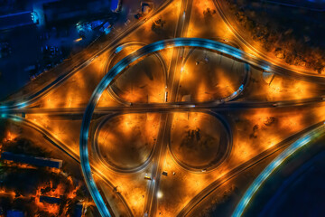 Road intersection, bridges, highways and car traffic in blurred speed motion, aerial top view at night.