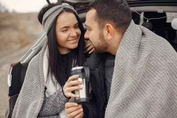 Cute couple in a field. Man in a black jacket. Family sitting on a trank.
