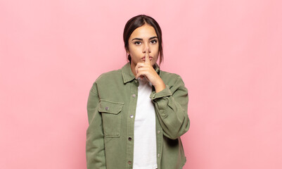 pretty young woman looking serious and cross with finger pressed to lips demanding silence or...