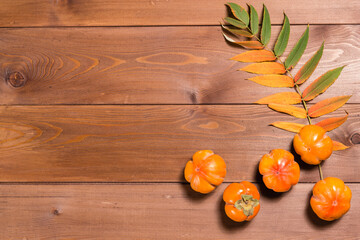 Abstract autumn still life: yellowed leaf and ripe persimmon on wooden table. Flat lay. Copy space