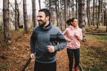 Young sporty cheerful couple running in woods and preparing for marathon. Man is faster then woman and he is winning.