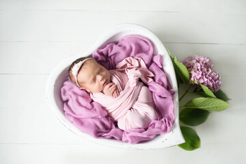 Little adorable newborn baby girl sleeps in a white wooden handmade heart decorated with flowers, newborn photo session
