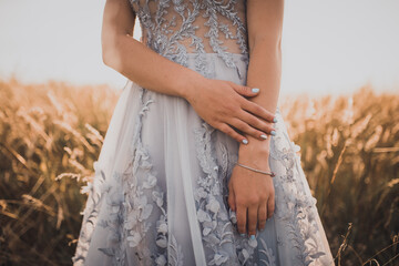 girl in a gray dress with flowers shows her beautiful blue manicure on a background of tall yellow...