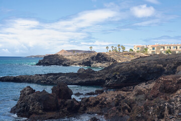 The black lava coast on the south coast of the Canary island of Tenerife. In the background is a small settlement in the village of 