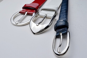 white, red, blue womens belts with glossy plaques on a white background.