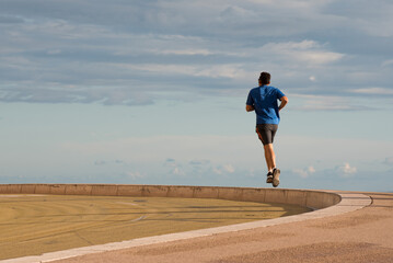 homme en bleu faisant de la course à pied seul sur la corniche suspendu entre terre et ciel 