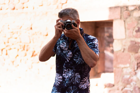 Front view of a man in Hawaiian shirt taking a photo with a vintage camera