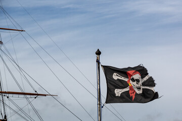 A jolly roger or skull and crossbones flag flying in front of the mast of an old ship