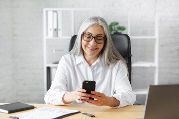 Senior grey-haired beautiful woman using smartphone and smiling. Happy businesswoman using mobile phone apps, texting message, browsing internet, shopping online. Mature people with mobile devices.