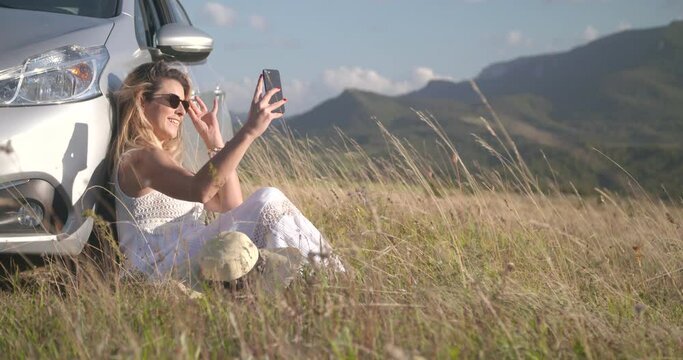 Young woman making a selfie picture in the sun in nature by the car