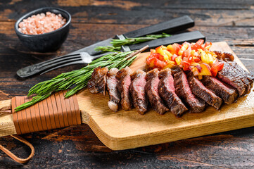 Grilled top sirloin cap or picanha steak on a cutting board with herbs. Dark wooden background. Top...