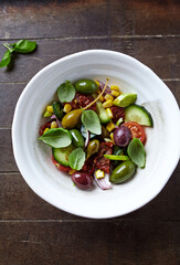 Simple Salad with Green and Kalamata Olives, Cucumber, Cherry and marinated Tomatoes, Capers and Jalapeno Pepper. Brown wooden background. Top view.  
