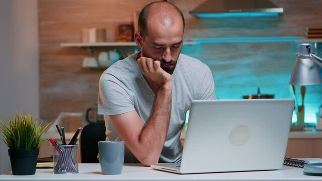 Stressed young business man sleeping in front of laptop in home kitchen. Busy exhausted remote employee napping on chair waking up working on laptop overtime using modern technology network wireless