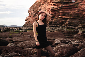 Girl posing with a n elegant black dress at a rocky cove of the basque coast.