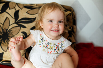 A 2 years old girl is sitting on the bed and smiling. The child rejoices and turns over. Happy child