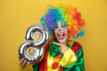 Clown standing over yellow insolated yellow background holding a number eight balloon. Anniversary