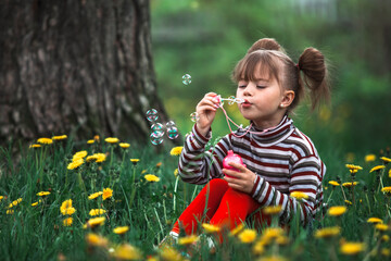 Little cute girl blowing soap bubbles in the park.