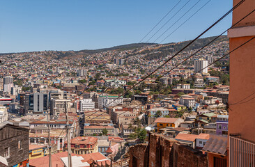 Valparaiso, Chile - December 8, 2008: Wide urban landscape over flanks of hills with hundreds of houses in all colors and shapes under blue sky. Green top of hills. Electrical wiring nearby.
