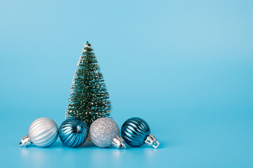 Photo of little toy fir tree and four beautiful baubles isolated over light blue color background with copy space